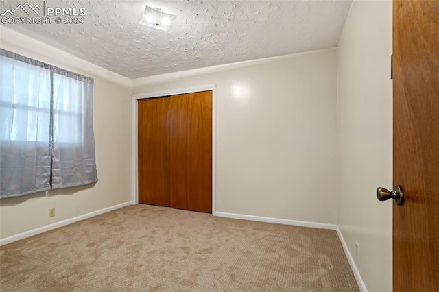 unfurnished bedroom featuring a closet, a textured ceiling, and light colored carpet