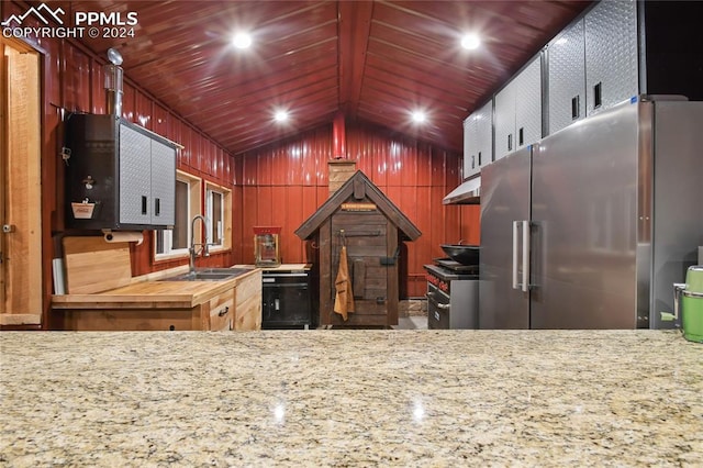 kitchen with butcher block counters, appliances with stainless steel finishes, wooden walls, sink, and lofted ceiling