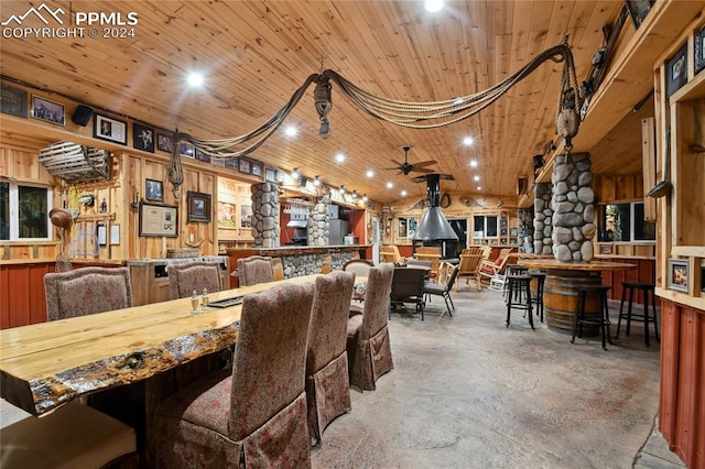 dining area featuring concrete floors, wood ceiling, wooden walls, and ceiling fan