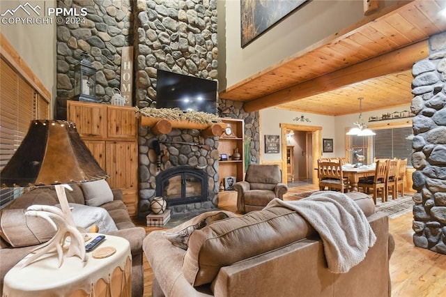 living room featuring light hardwood / wood-style floors, beam ceiling, a stone fireplace, wood ceiling, and a chandelier