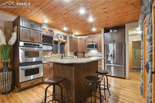 kitchen with wooden ceiling, a breakfast bar, appliances with stainless steel finishes, and light hardwood / wood-style flooring