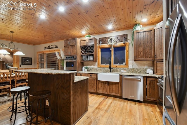 kitchen with stainless steel appliances, light stone counters, sink, light wood-type flooring, and decorative light fixtures