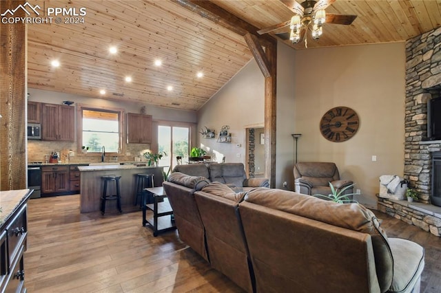 living room featuring wood ceiling, high vaulted ceiling, ceiling fan, a fireplace, and light hardwood / wood-style flooring