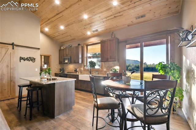 kitchen with light hardwood / wood-style floors, vaulted ceiling, a barn door, sink, and a kitchen island