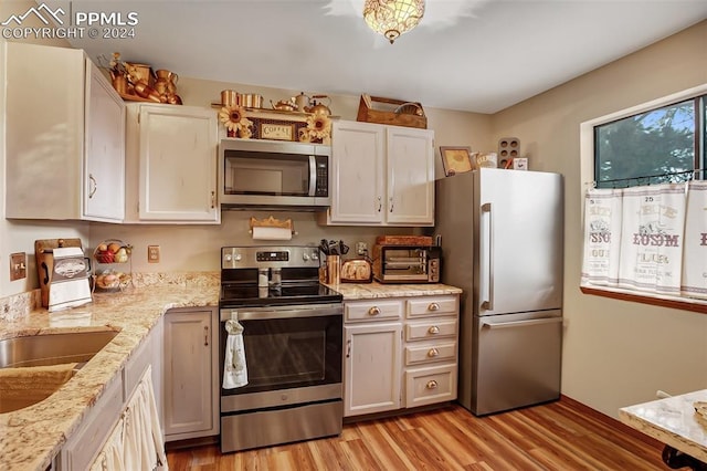 kitchen with light wood-type flooring, appliances with stainless steel finishes, light stone countertops, sink, and white cabinets