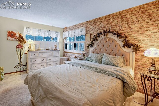 bedroom featuring a textured ceiling, brick wall, and light carpet