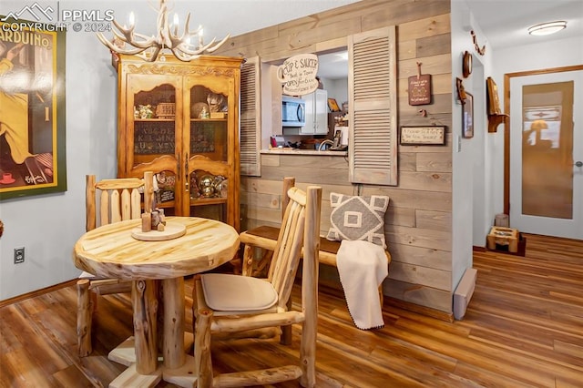 dining area with a chandelier, wooden walls, and hardwood / wood-style flooring