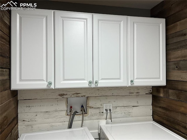 clothes washing area with wooden walls, cabinets, and washer hookup