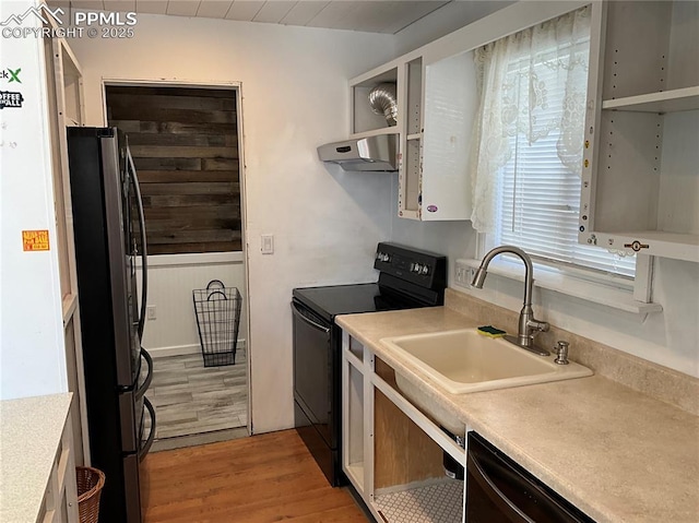 kitchen with sink, light hardwood / wood-style floors, wooden walls, and black appliances