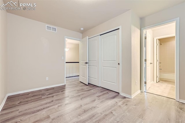 unfurnished bedroom featuring a closet, ensuite bathroom, and light wood-type flooring