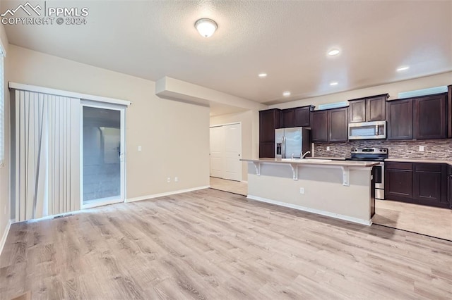 kitchen featuring light hardwood / wood-style floors, a breakfast bar, stainless steel appliances, and a center island with sink