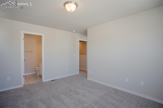 unfurnished bedroom featuring a spacious closet, connected bathroom, and light colored carpet