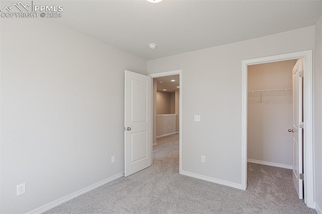 unfurnished bedroom featuring a walk in closet, a closet, and light colored carpet