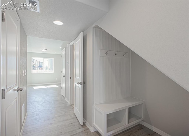 mudroom featuring a textured ceiling, vaulted ceiling, and light wood-type flooring