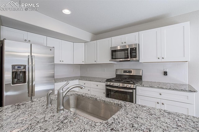 kitchen with light stone countertops, appliances with stainless steel finishes, sink, white cabinetry, and decorative backsplash