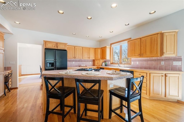 kitchen featuring a center island, light hardwood / wood-style flooring, tasteful backsplash, and black fridge