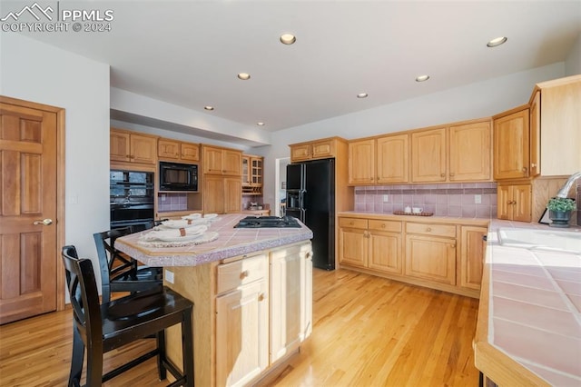 kitchen featuring decorative backsplash, tile countertops, sink, black appliances, and a center island