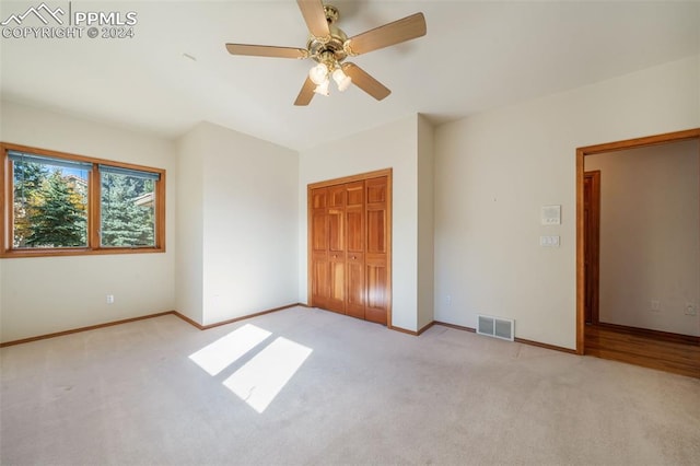 unfurnished bedroom with light colored carpet, a closet, and ceiling fan