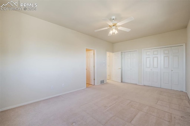 unfurnished bedroom with two closets, light colored carpet, and ceiling fan