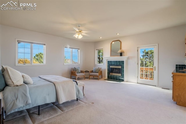 bedroom with access to outside, a tiled fireplace, light colored carpet, and ceiling fan