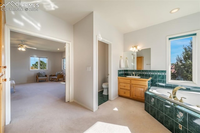 bathroom with vanity, toilet, tiled tub, and ceiling fan