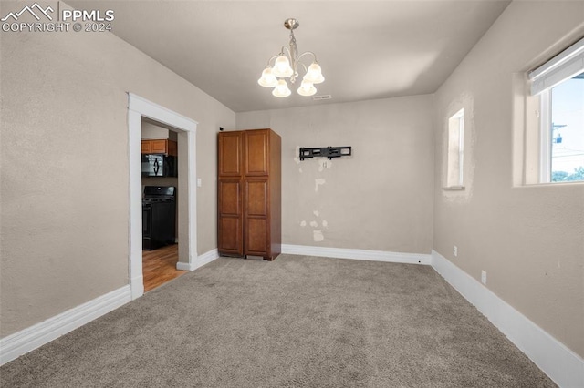 spare room featuring light carpet and an inviting chandelier