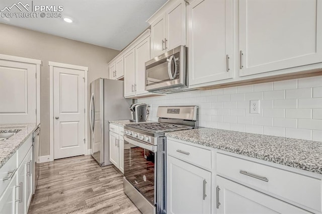 kitchen with tasteful backsplash, white cabinetry, appliances with stainless steel finishes, light stone countertops, and light hardwood / wood-style floors