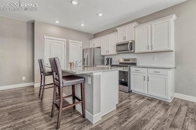 kitchen featuring a kitchen island with sink, a kitchen bar, appliances with stainless steel finishes, and white cabinetry