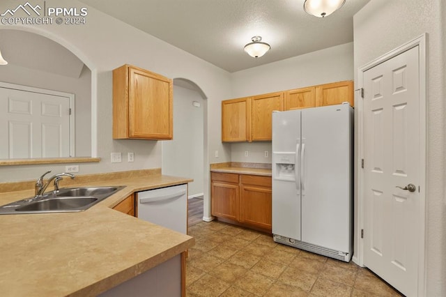 kitchen featuring a textured ceiling, light brown cabinetry, sink, and white appliances