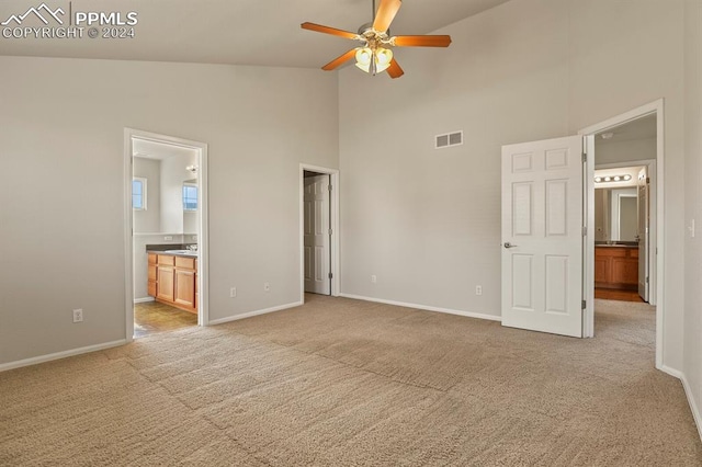 unfurnished bedroom featuring ensuite bath, ceiling fan, high vaulted ceiling, and light carpet