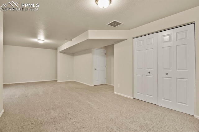 basement featuring light carpet and a textured ceiling