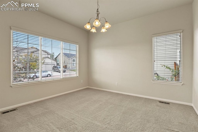 carpeted empty room featuring a wealth of natural light and a notable chandelier