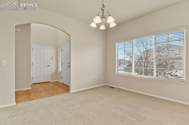 carpeted empty room featuring plenty of natural light and an inviting chandelier