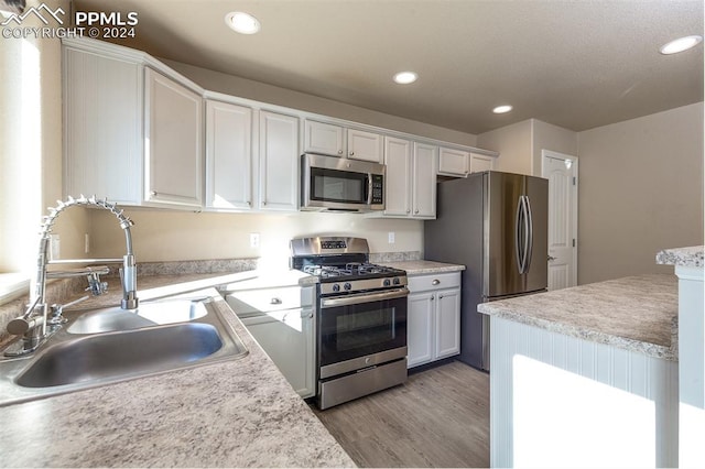 kitchen featuring white cabinetry, appliances with stainless steel finishes, sink, and light wood-type flooring