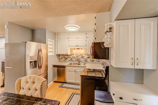 kitchen featuring tasteful backsplash, appliances with stainless steel finishes, white cabinetry, light hardwood / wood-style flooring, and sink