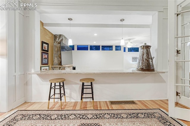 kitchen with ceiling fan, a breakfast bar, decorative light fixtures, and light wood-type flooring