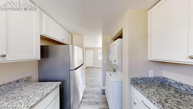 kitchen featuring light stone countertops, light wood-type flooring, stainless steel fridge, white cabinetry, and stacked washer and dryer