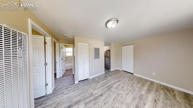 unfurnished bedroom featuring light hardwood / wood-style floors, electric panel, two closets, and stainless steel refrigerator