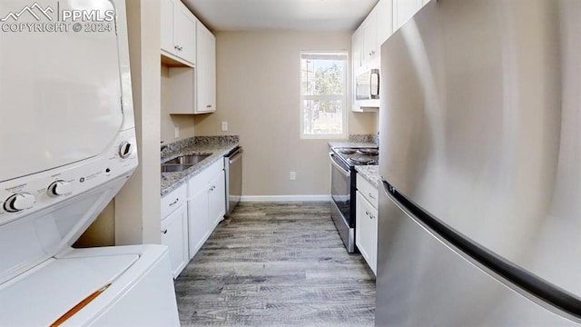 kitchen featuring stacked washer / drying machine, light stone countertops, light wood-type flooring, white cabinetry, and appliances with stainless steel finishes