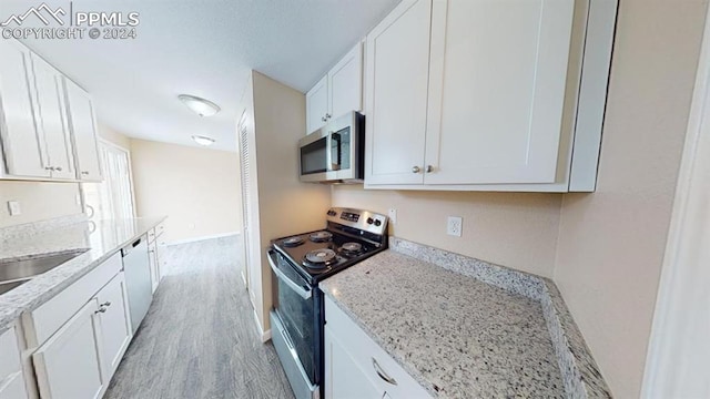 kitchen with appliances with stainless steel finishes, white cabinets, light stone counters, and light hardwood / wood-style floors