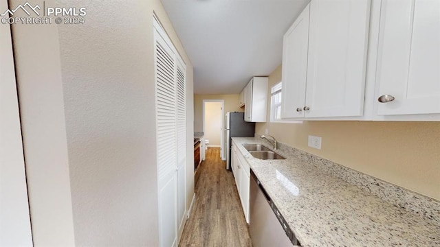 kitchen with stainless steel fridge, white cabinetry, light wood-type flooring, sink, and light stone counters