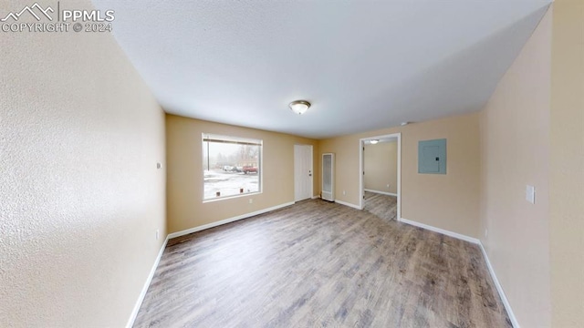 empty room with electric panel and wood-type flooring