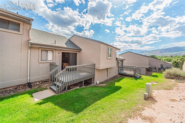 rear view of house featuring a deck with mountain view and a lawn