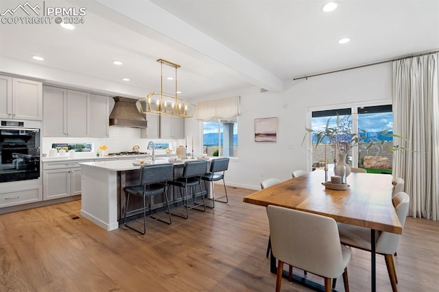 kitchen featuring custom range hood, light hardwood / wood-style floors, a wealth of natural light, and hanging light fixtures