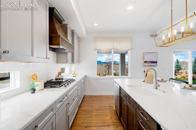 kitchen with sink, a healthy amount of sunlight, decorative light fixtures, and custom exhaust hood