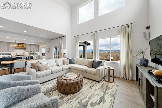 living room with a towering ceiling, an inviting chandelier, and light wood-type flooring