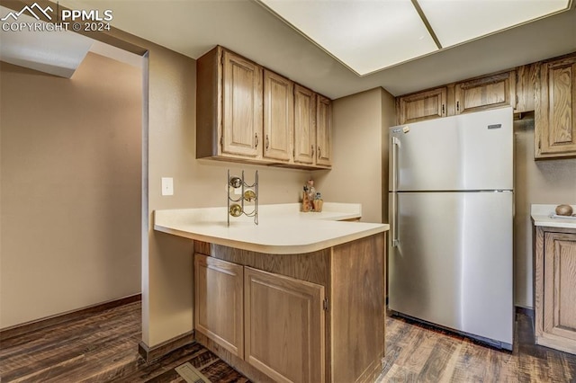 kitchen with dark wood-type flooring, stainless steel refrigerator, and kitchen peninsula