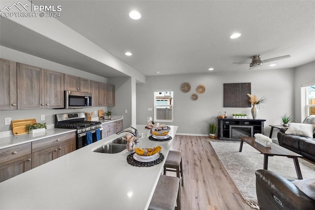 kitchen featuring appliances with stainless steel finishes, sink, a fireplace, light hardwood / wood-style floors, and ceiling fan