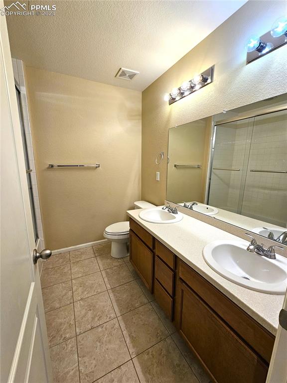 bathroom featuring a shower with door, a textured ceiling, toilet, vanity, and tile patterned flooring