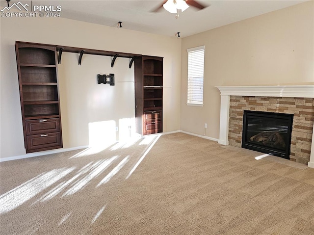 unfurnished living room with ceiling fan, a stone fireplace, and carpet floors